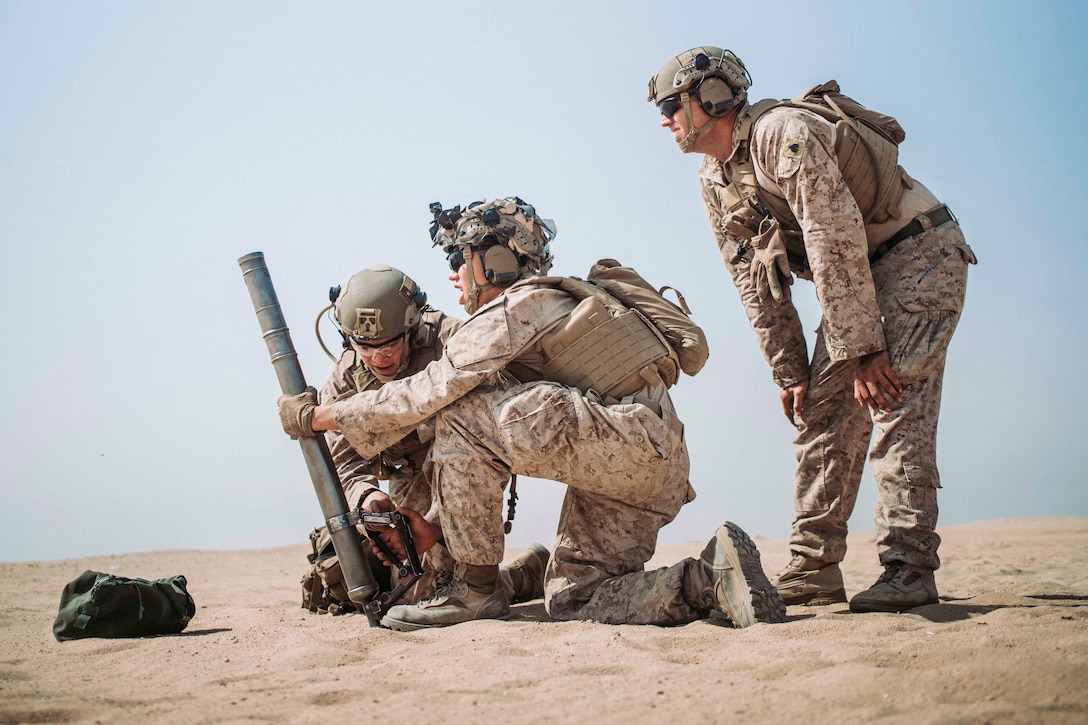 Two Marines prepare to fire a hand-held mortar system as another Marine watches.