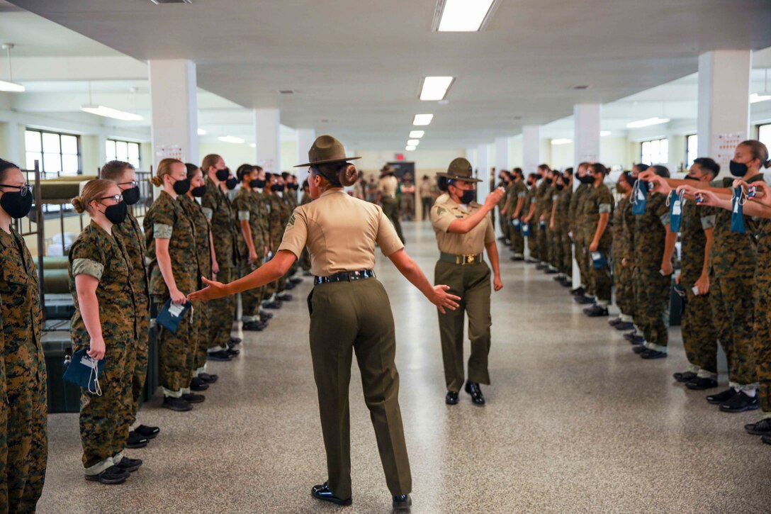 Marine Corps recruits stand in two lines facing each other as two Marines walk in between.