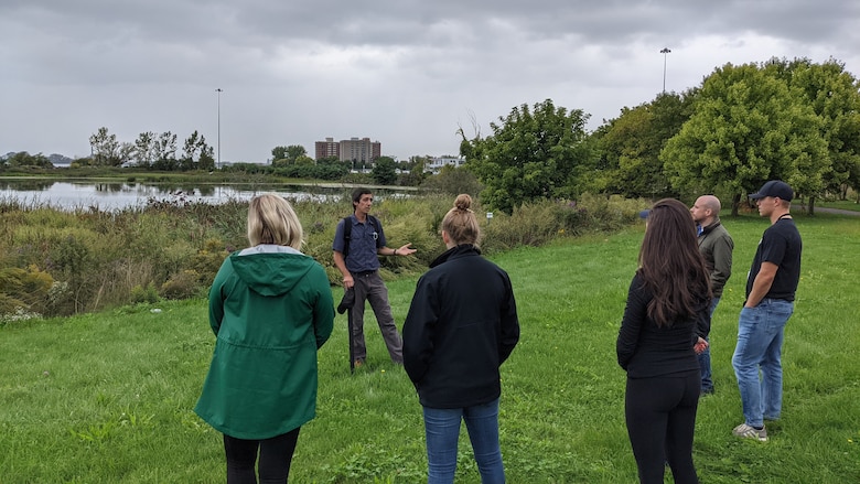 People standing on a grassy shoreline next to a wetland pond.