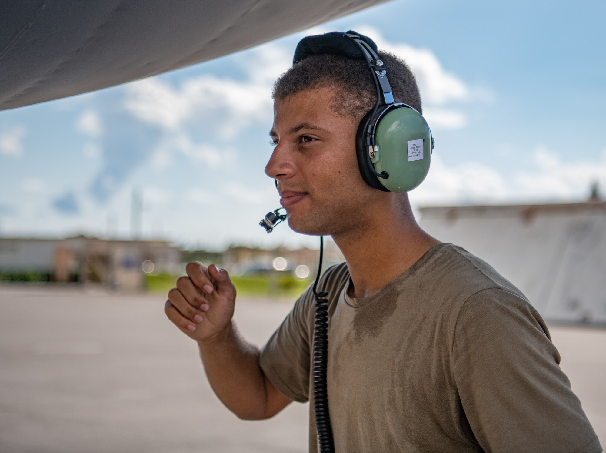 An Airman squats while talking on a headset.