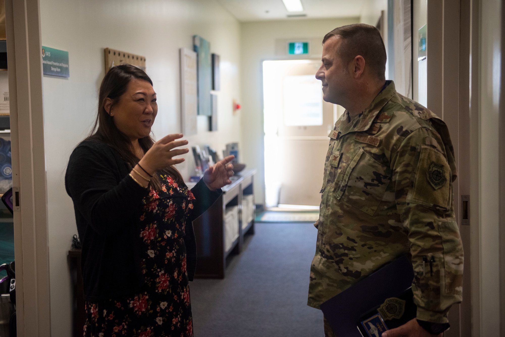 Man in military uniform stands and talks to female in an office.