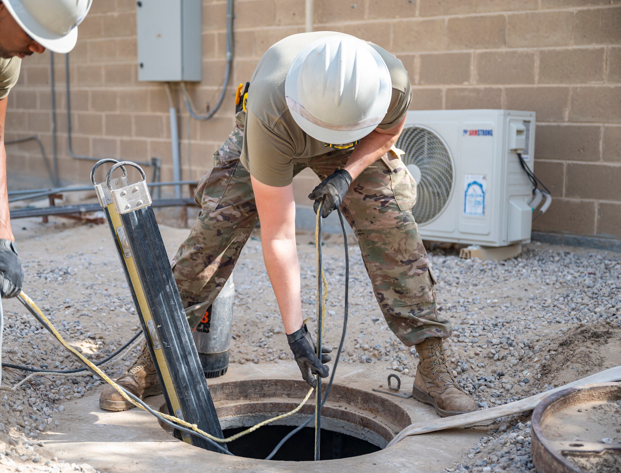 A member of the U.S. Air Forces Central, Air Force Forces A67 Engineering and Installation team lowers equipment into a communications maintenance hole at Ali Al Salem Air Base, Kuwait, Oct. 19, 2021.