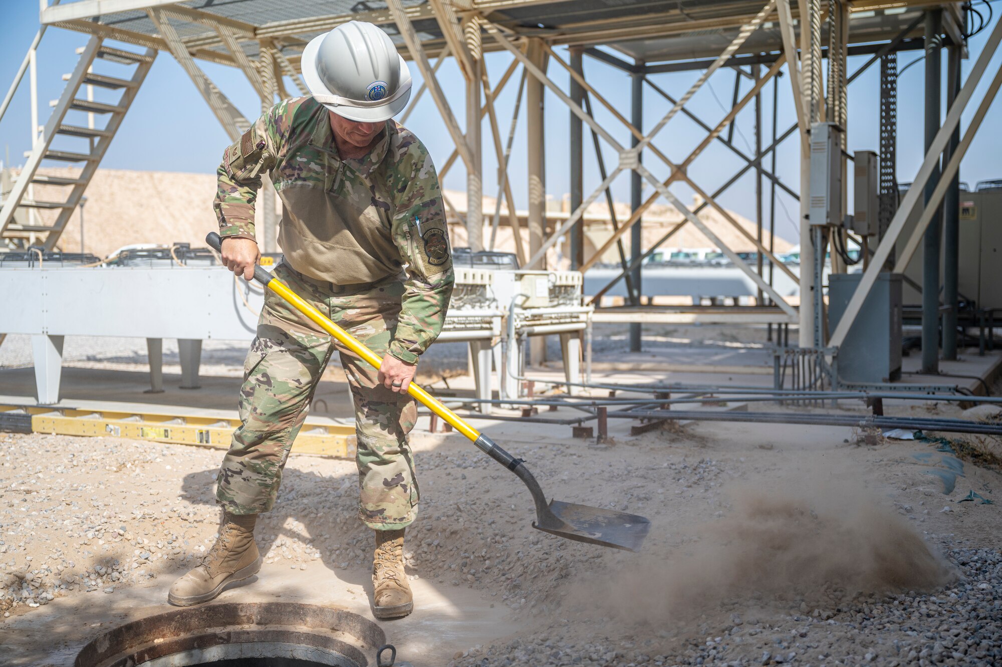 A member of the U.S. Air Forces Central, Air Force Forces A67 Engineering and Installation team removes dirt around the entrance to a communications maintenance hole at Ali Al Salem Air Base, Kuwait, on Oct. 19, 2021.