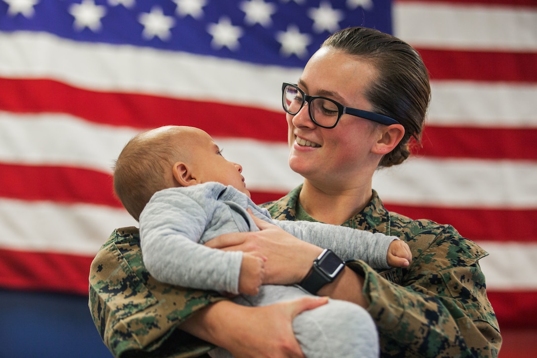 A Marine smiles as she looks down at a baby she is holding.