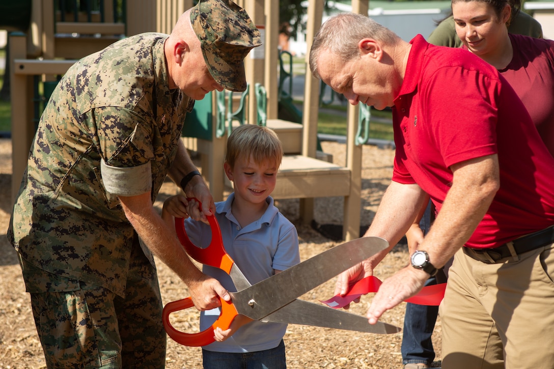 A Marine Corps officer helps a child cut a ribbon with a large pair of scissors.