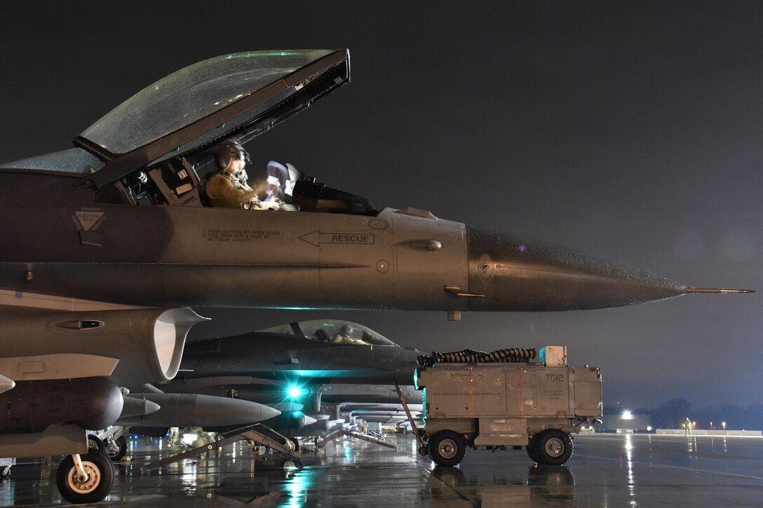 A line of military aircraft are prepared for flight at night.