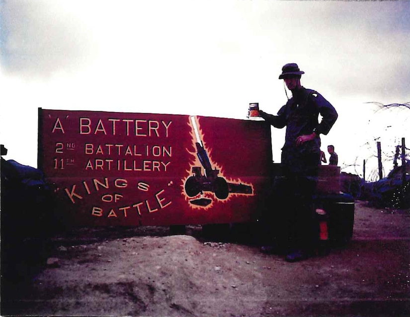 Retired Lt. Col. Dick Stoops, seen here as a captain, stands next to his battery sign eating peaches on Firebase Sledge, Vietnam in 1969 (Photo courtesy of Retired Lt. Col. Dick Stoops).