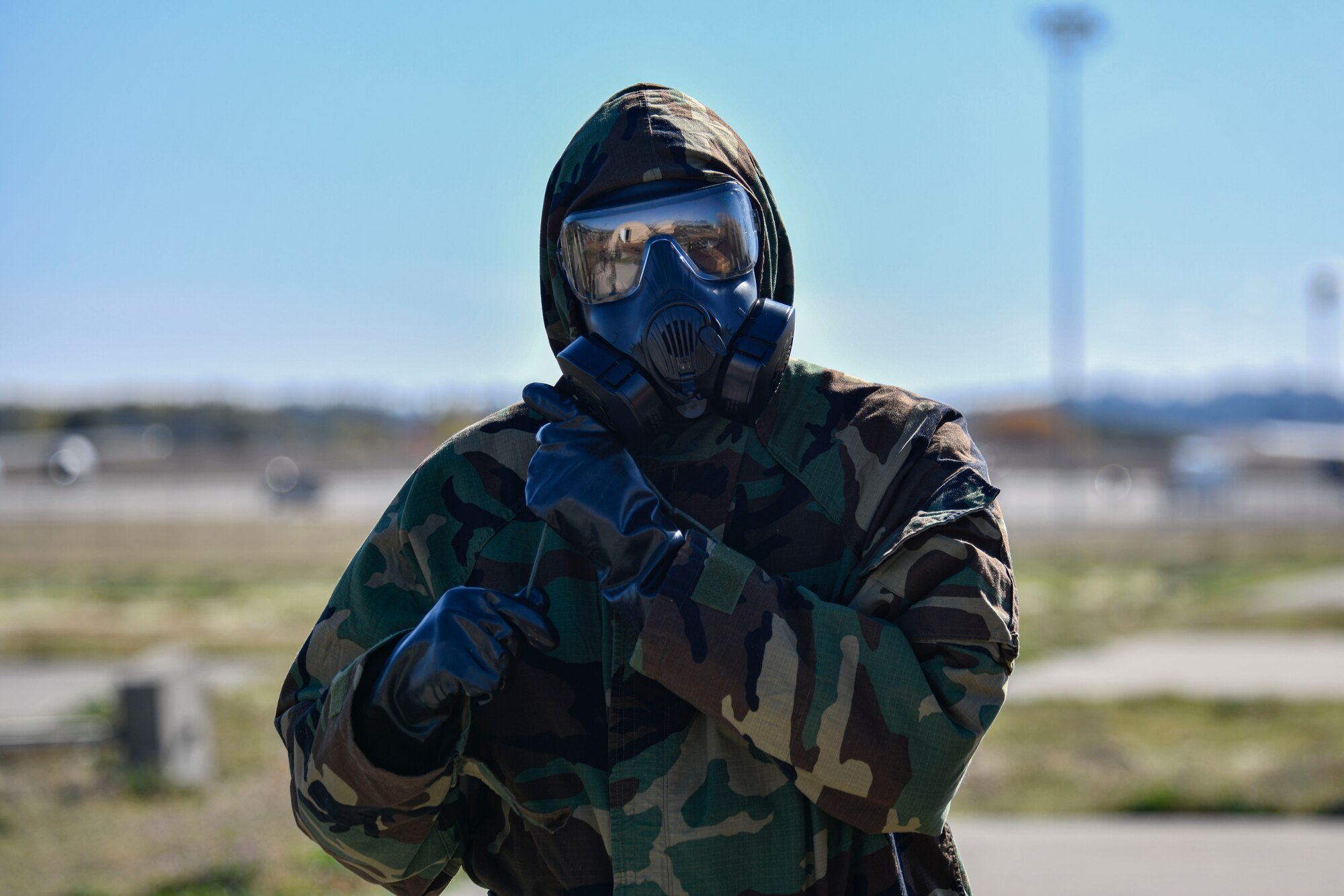U.S. Air Force Airman from Team Fairchild tightens the draw string fastening on their Mission Oriented Protective Posture equipment during a large readiness exercise at Fairchild Air Force Base, Washington, Oct. 7, 2021. The scenario required Airmen to properly don their gear during a chemical, biological, radiological and nuclear attack scenario. (U.S. Air Force photo by Senior Airman Ryan Gomez)