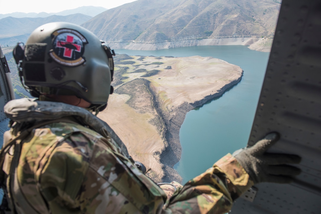 A person looks out of an open helicopter door onto a river and the hills below.