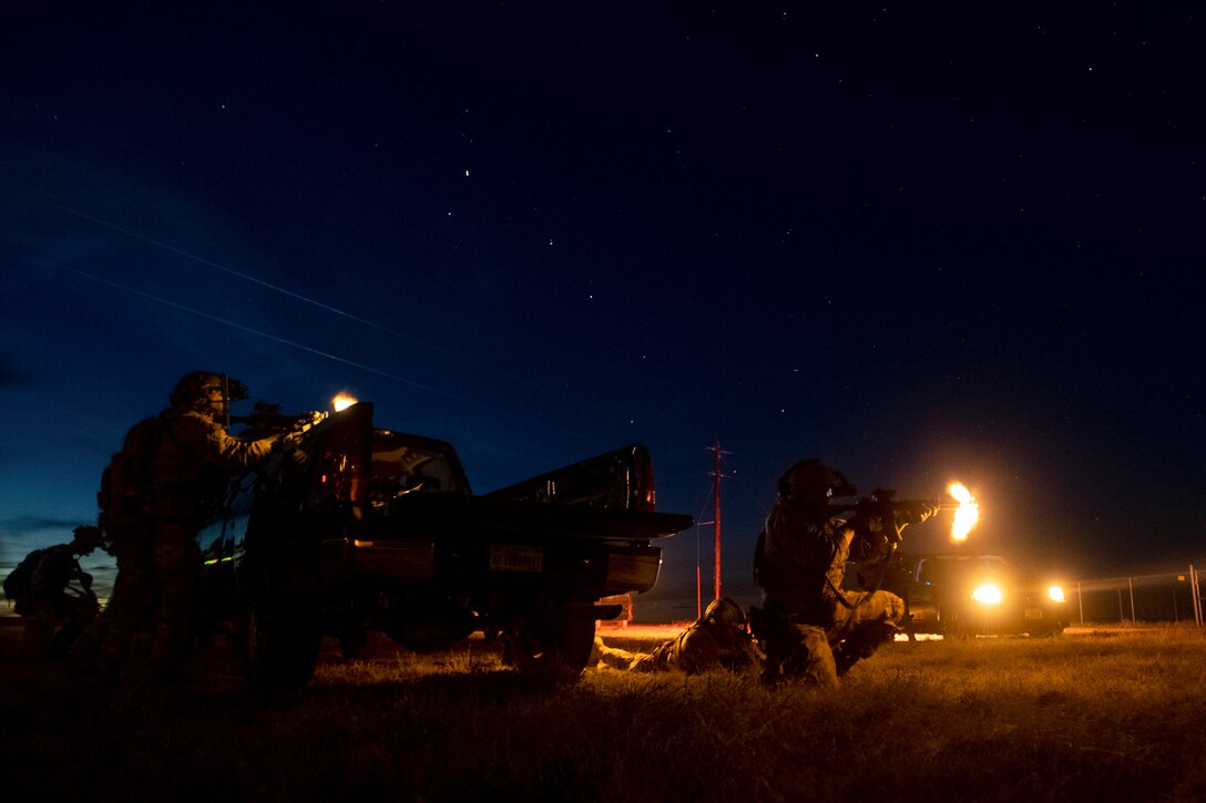 Airmen fire weapons near vehicles under a starry sky.