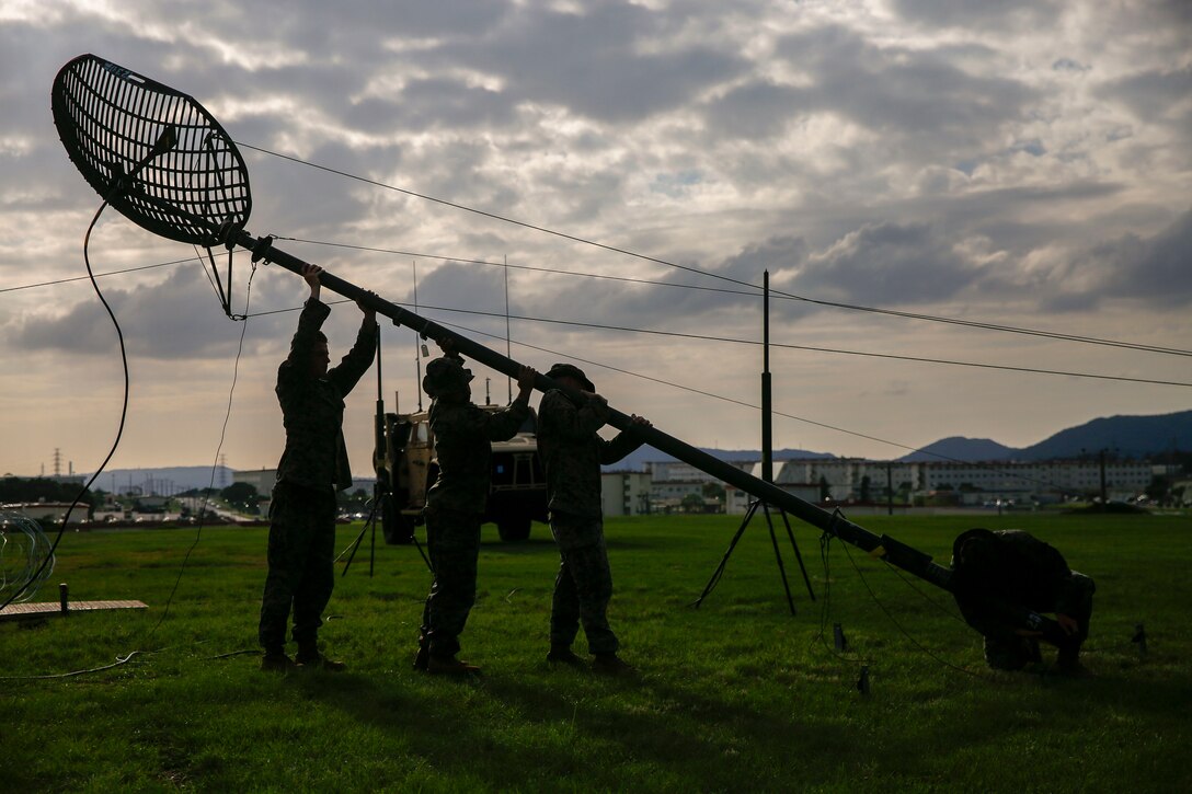 Three Marines lift a satellite near power lines in a field.