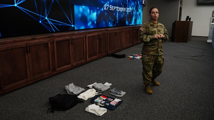 A woman stands at the head of a room; beside her, a number of items are laid out on the floor.