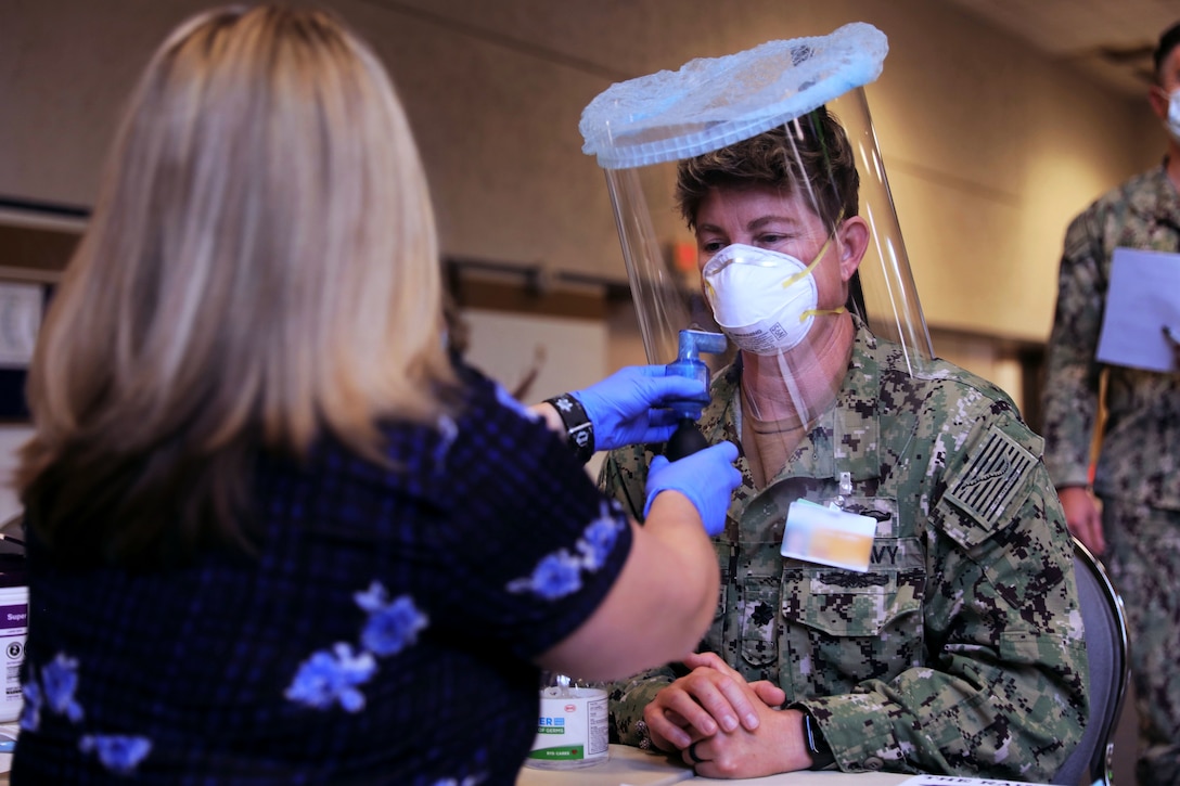 A woman holding a small bottle fit tests a soldier for a respirator mask.