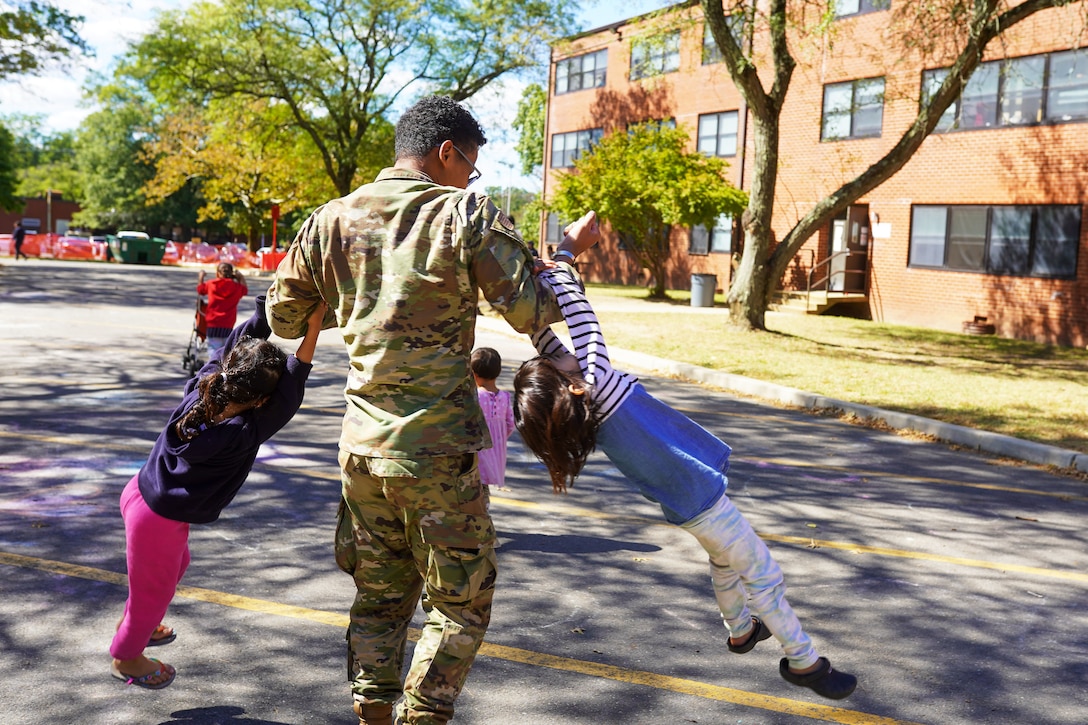 An airman plays with two Afghan children by letting them swing on each of his arms.