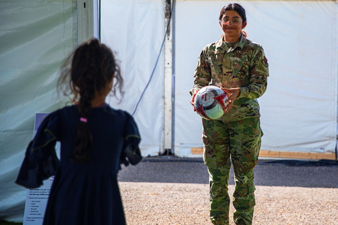An airman smiling and holding a ball plays catch with an Afghan child.