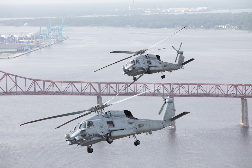 Two helicopters flying over bridge.