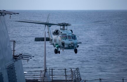 Helicopter flying over side of ship.