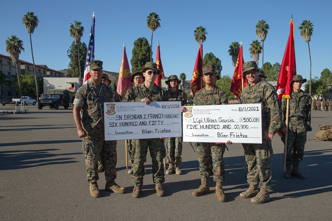 U.S. Marine Corps Col. Siebrand H. Niewenhous, commanding officer, 1st Supply Battalion, 1st Marine Logistics Group, presents LSSN Brendan Franco, an additive manufacturing engineer, and Lance Cpl. Garcia Ulises, a distribution management specialist, with an Innovation Awards Program check, after a 12-mile battalion hike on Camp Pendleton, California, Oct. 1 2021.