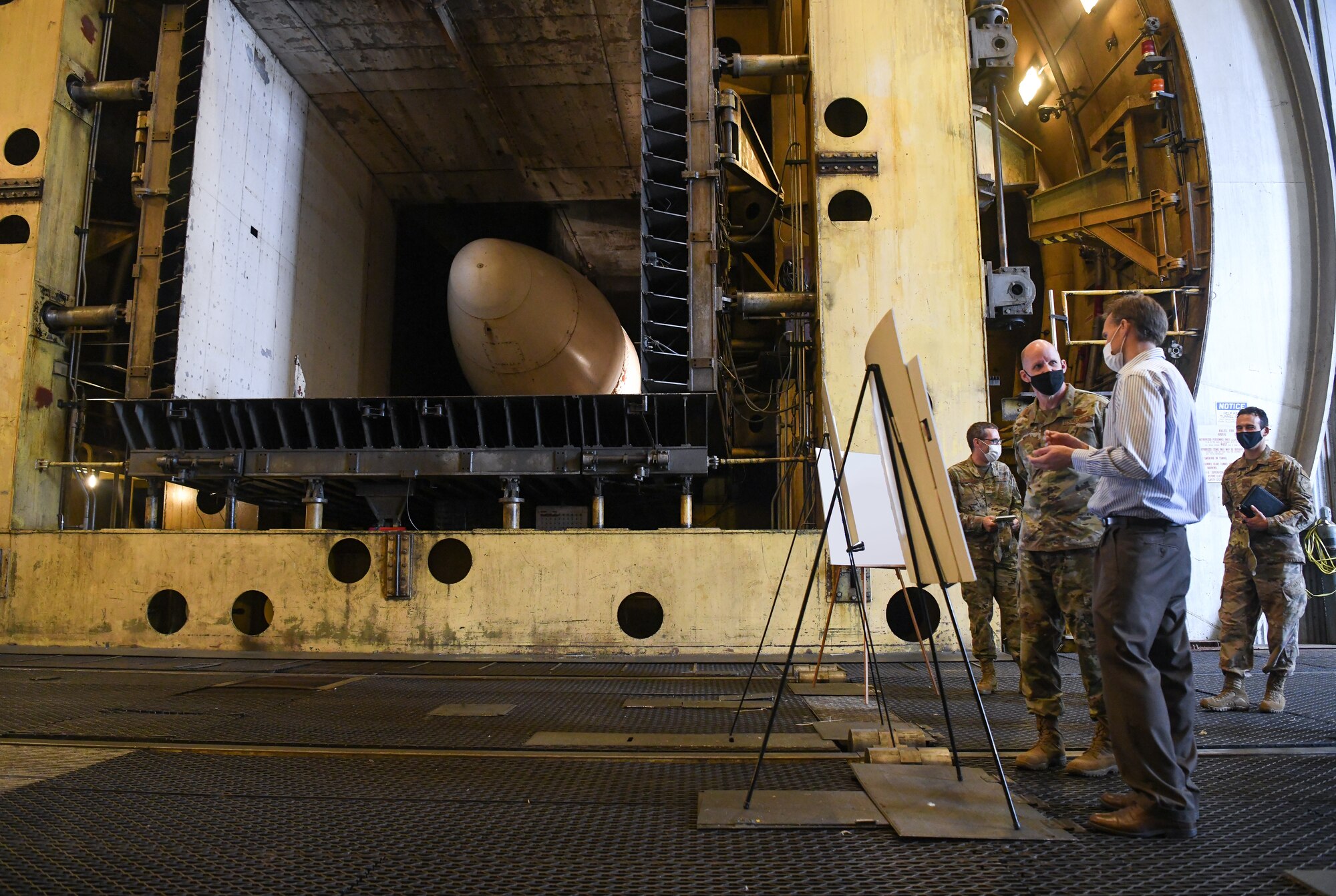 Dr. Rich Roberts, second from right, chief of the Aerodynamics Branch Store Separation Section of Arnold Engineering Development Complex (AEDC), briefs Maj. Gen. Evan Dertien, commander, Air Force Test Center, on the 16-foot transonic wind tunnel during Dertien's visit to Arnold Air Force Base, headquarters of AEDC, Oct. 13, 2021. The transonic tunnel is part of the Aerodynamics Test Branch of AEDC, which provides aerodynamic effects and captive trajectory ground-test capabilities. (U.S. Air Force photo by Jill Pickett) (This image has been altered by obscuring a poster for security reasons.)