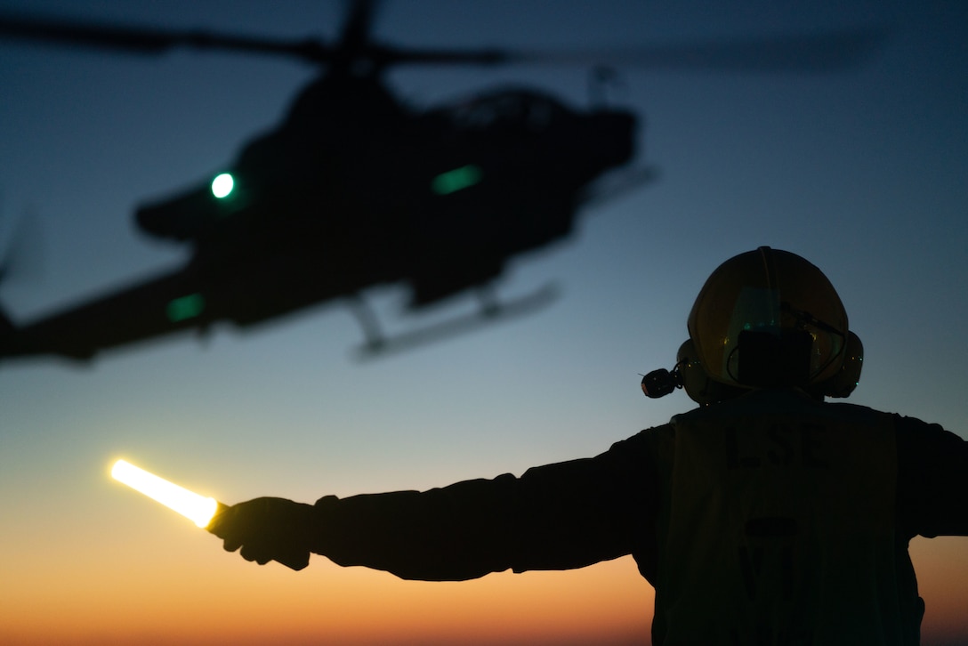 U.S. Navy Aviation Boatswains Mate Handling 3rd Class Israel Avalos, assigned to amphibious assault ship USS Kearsarge (LHD 3), signals an AH-1 Cobra for landing during flight operations, Oct. 20. The 22nd MEU and Amphibious Squadron Six is underway for PHIBRON-MEU Integrated Training in preparation for an upcoming deployment. PMINT is the first at-sea period in the MEU's Predeployment Training Program; it aims to increase interoperability and build relationships between Marines and Sailors.
