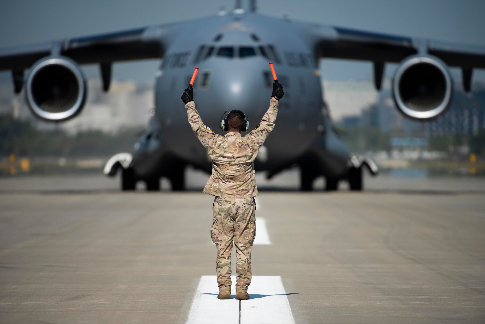 A U.S. Air Force Airman, assigned to the 535th Airlift Squadron based at Joint Base Pearl-Harbor Hickam, Hawaii, marshalls a C-17 Globemaster III at Seoul Air Base, Republic of Korea, following an aerial demonstration as part of the Seoul International Aerospace and Defense Exhibition 2021, Oct. 18. During the 5-day ADEX, attendees can experience aerial and ground demonstrations, learn about a variety of aerospace and defense technologies during daily seminars, and view a multitude of U.S. and ROK static displays. (U.S. Air Force photo by Staff Sgt. Gabrielle Spalding)