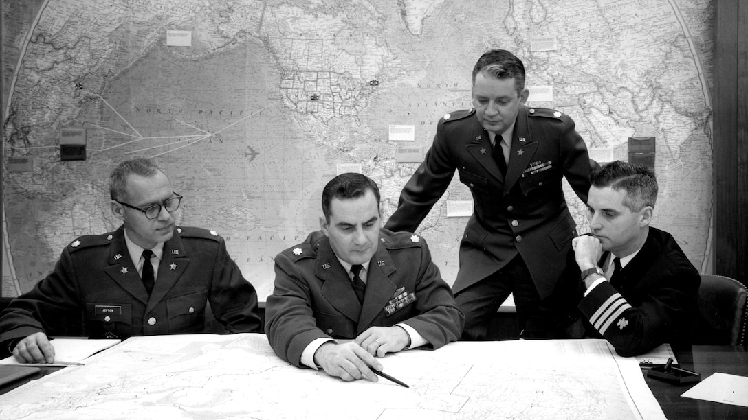 Four male military officers view a map in 1964.