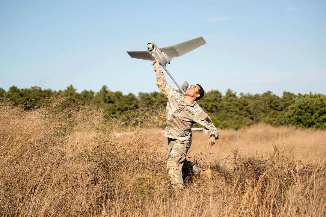 A soldier launches an unmanned aerial vehicle into the air while running a field.