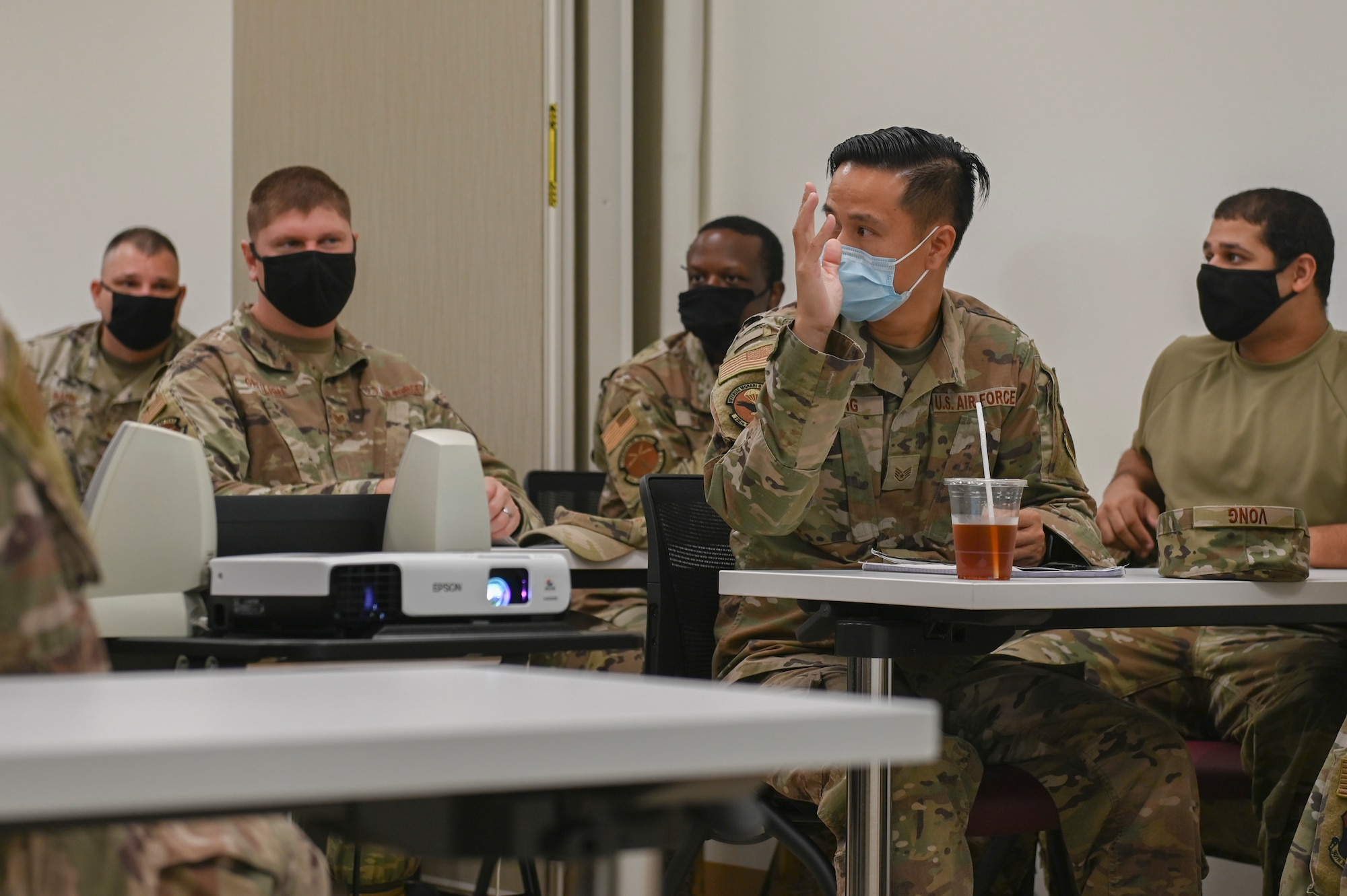 A military member raises his hand while looking behind him.