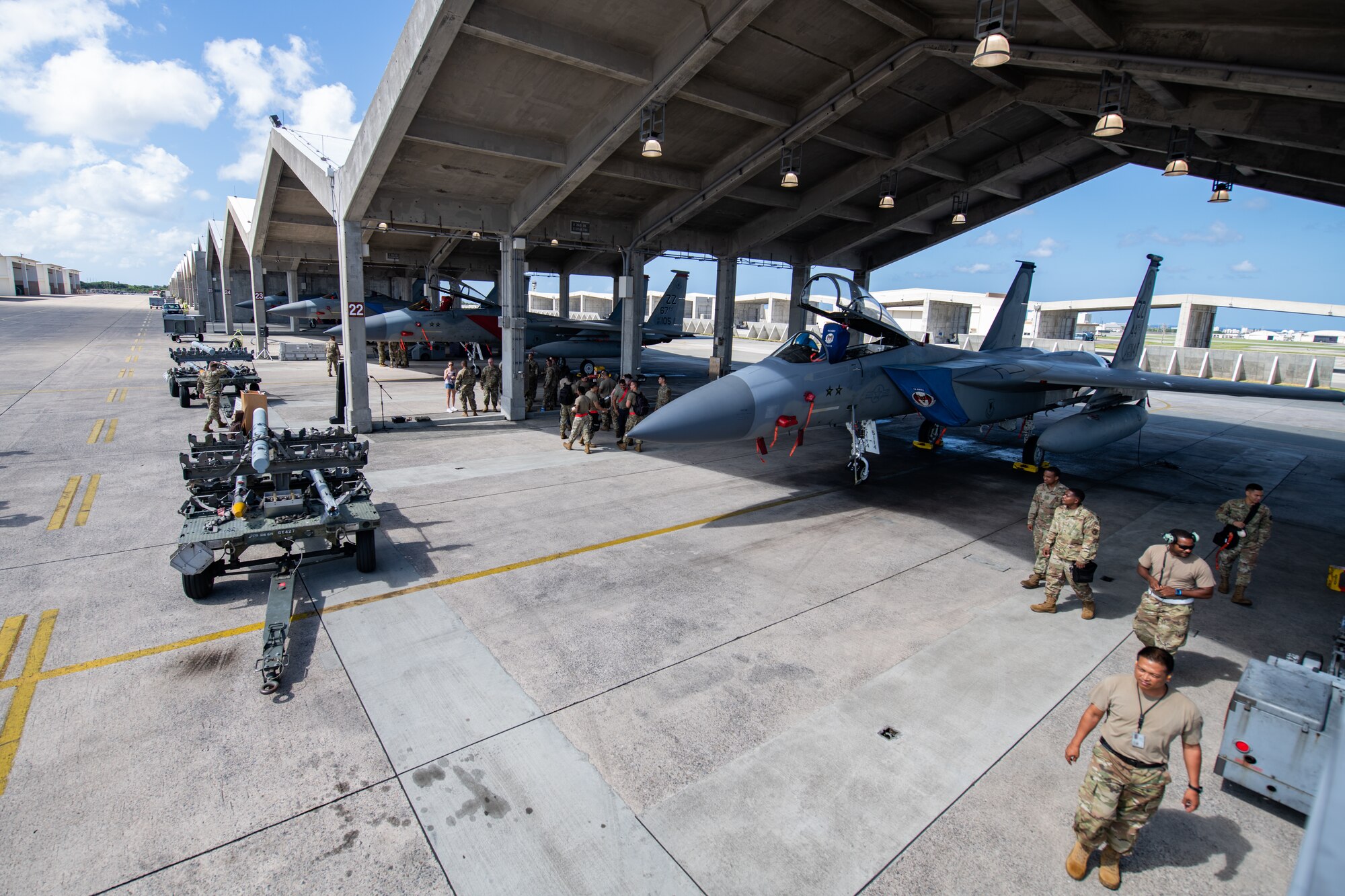Fighter jets and maintenance workers wait under hangars to begin a load competition underneath the bright sun.