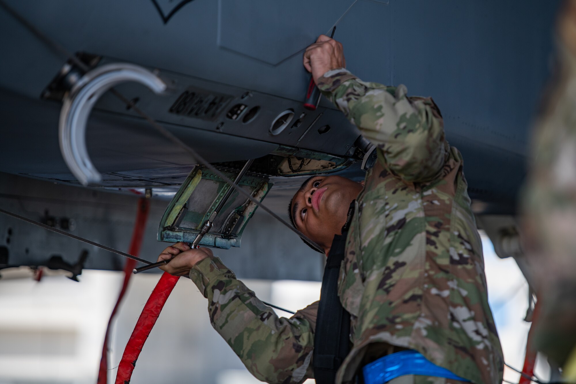 An airman tightens bolts underneath a fighter jet.