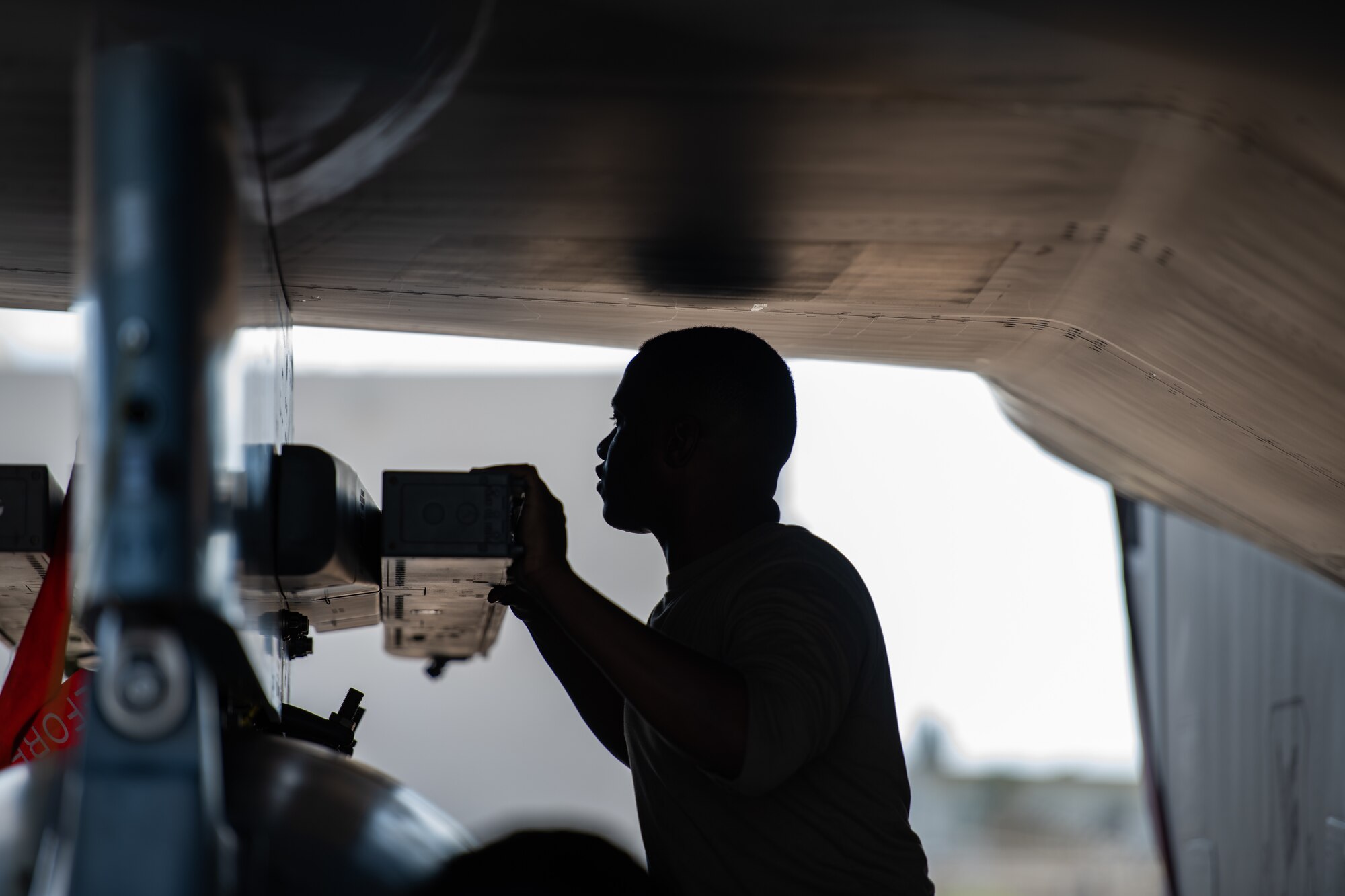 An airman under an F-15C Eagle checks a rack underneath the wing.
