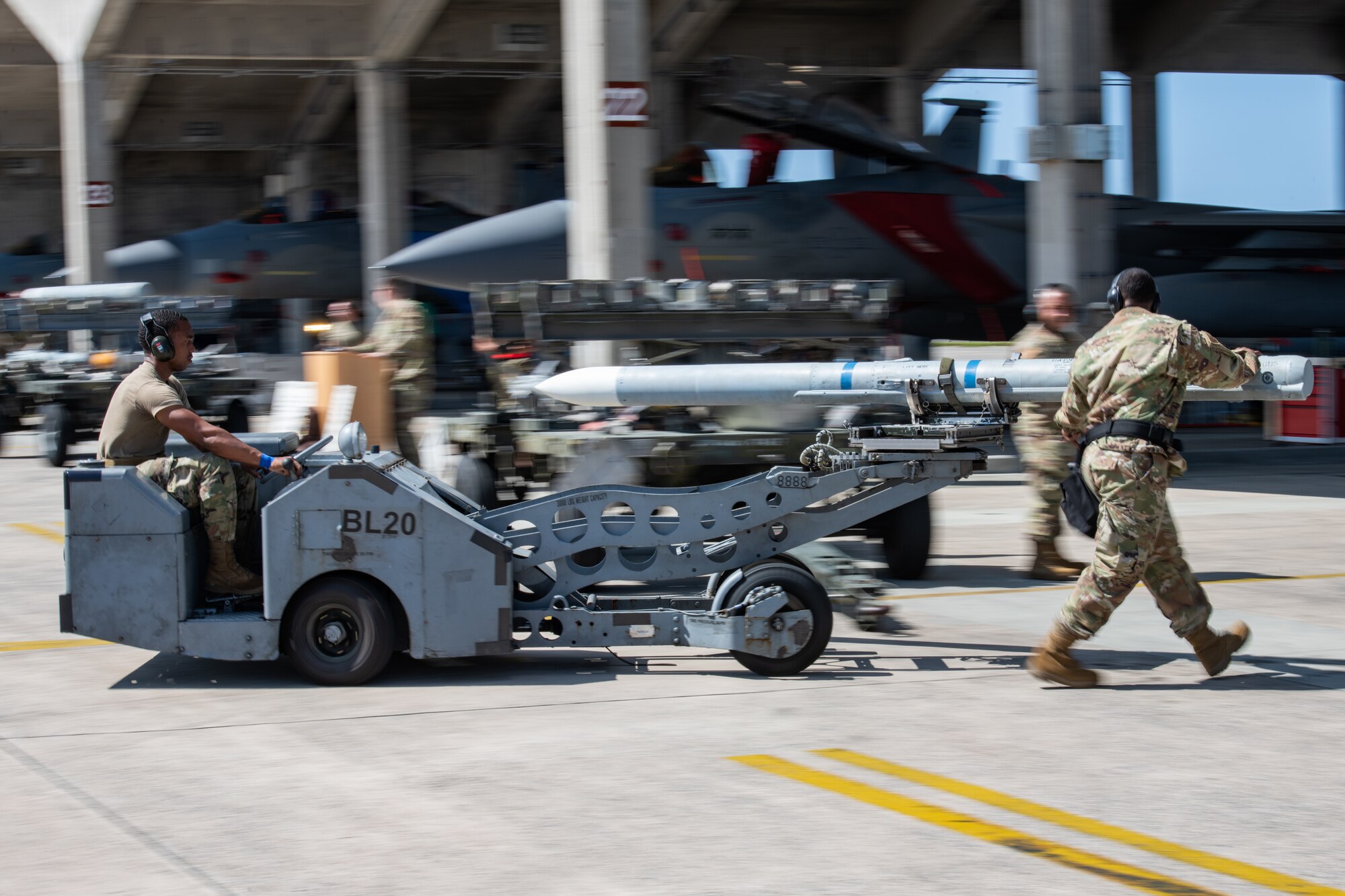 An airman maneuvers a machine carrying a missile with the help of another airman