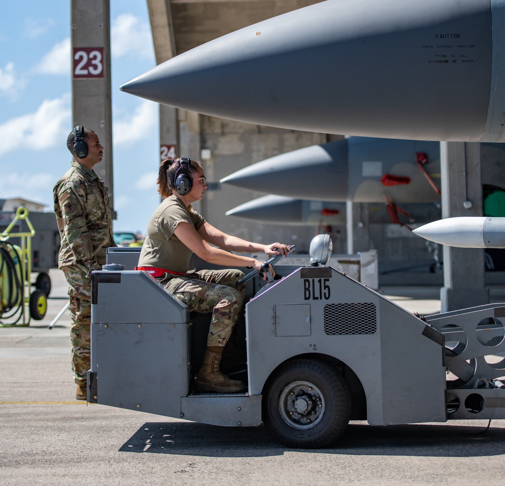A female Airman steers a machine that carries a missile toward a fighter jet.