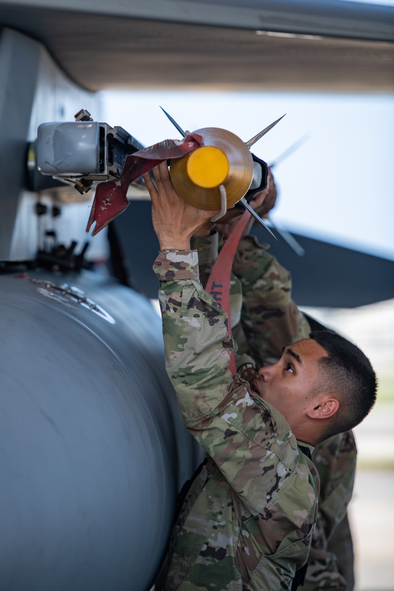An Airman along with his two teammates puts attaches a missile underneath the wing of a fighter jet.