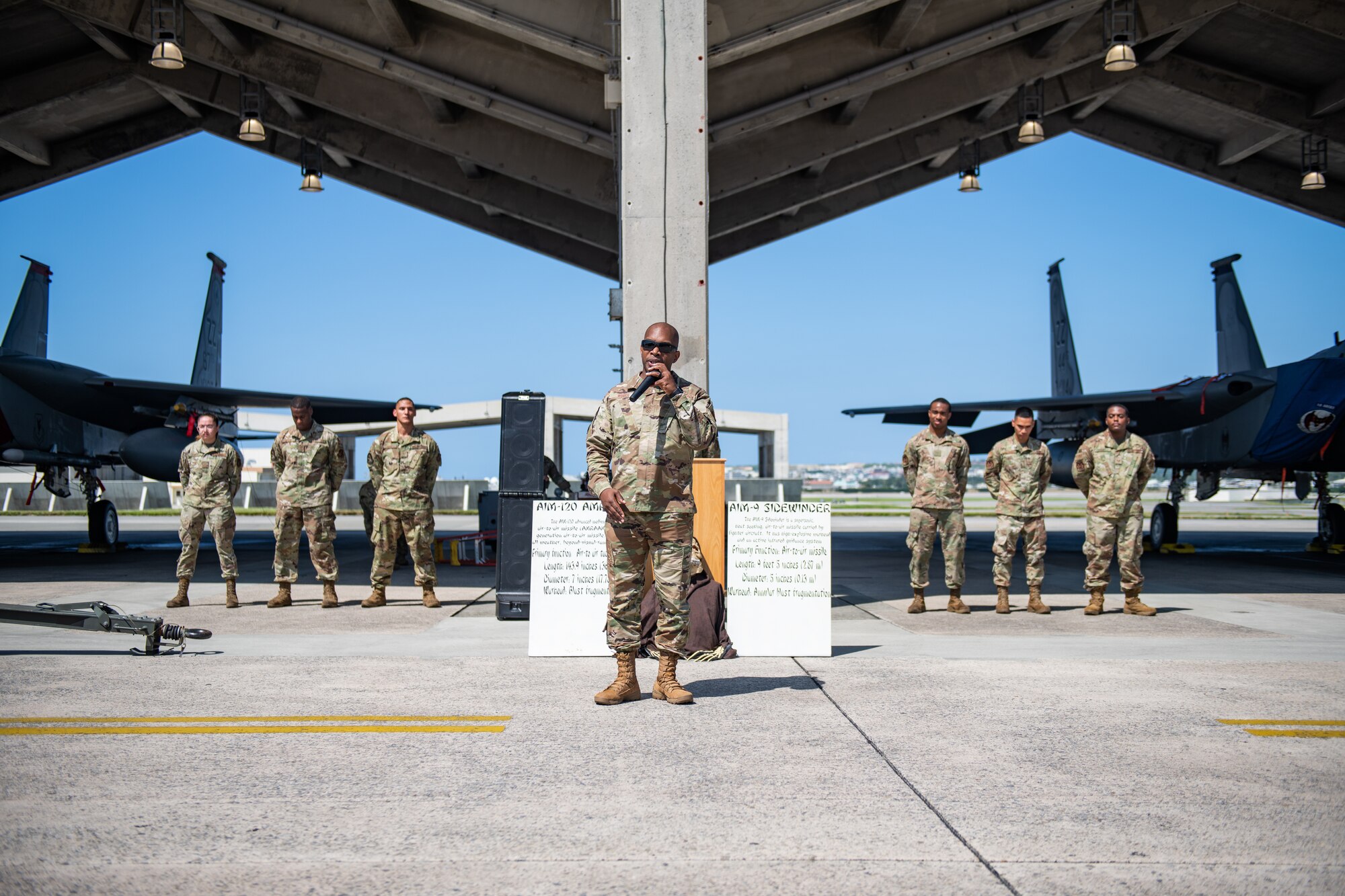 An Airman stands framed by two teams of three maintainers and two fighter jets.