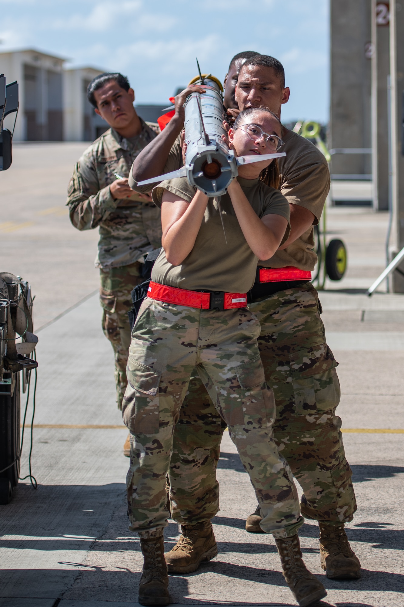3 Airmen carry a missile while an evaluator watches from behind