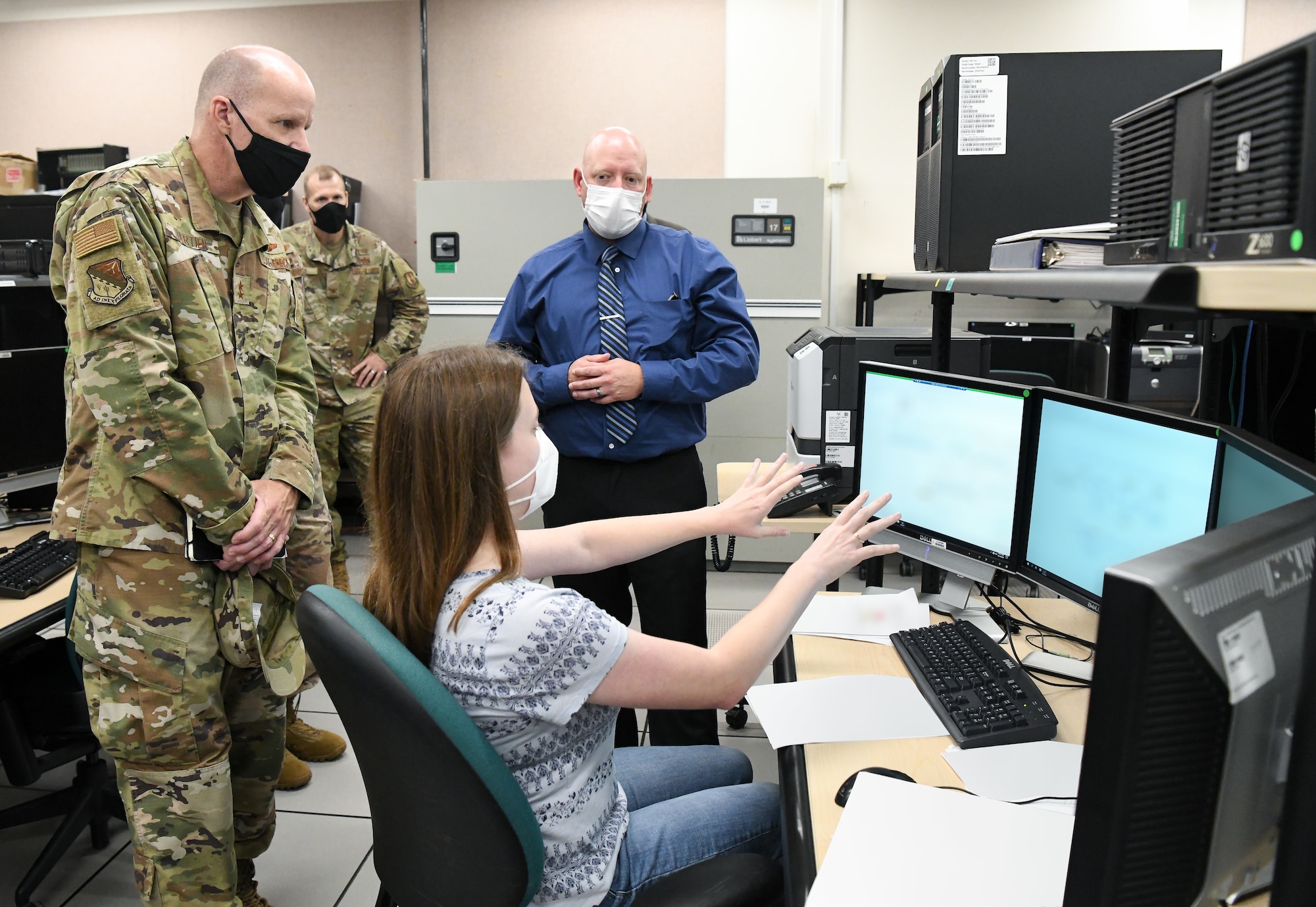 Mary Keen, center, a facility modeling engineer, explains how Arnold Engineering Development Complex test facility operations are simulated in the Range Systems Support Lab to Maj. Gen. Evan Dertien, commander, Air Force Test Center, during Dertien's visit to Arnold Air Force Base, Oct. 14, 2021. Also pictured, from left, are Col. Robert Lance, director of the Test Support Division, and Scott Howard, Test Information Systems Section chief. (U.S. Air Force photo by Jill Pickett) (This image has been altered by obscuring screens and papers for security purposes.)