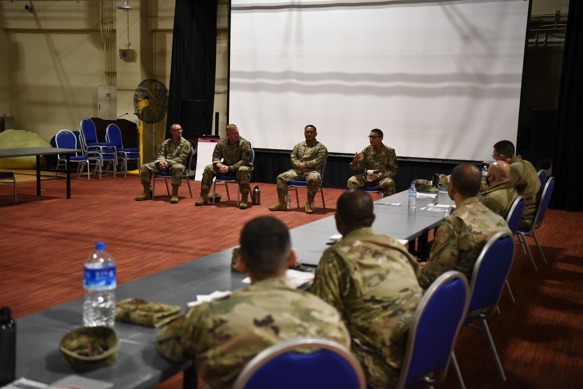 Four military members sit as a panel in front of other military members.