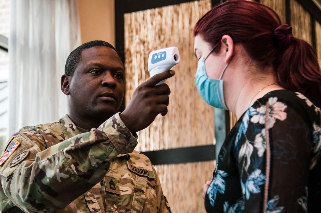 A soldier uses a thermometer to check the body temperature of an airman.