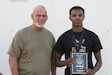 Spc. Yacob I. Warsame, a signal support systems specialist assigned to 3rd Expeditionary Sustainment Command, stands with Roger Disbrow, the morale, welfare, and recreation director, after placing second in the Army Ten-Miler Shadow Run at Camp Arifjan, Kuwait, on Oct. 10, 2021. The Denver, Colo., native, currently deployed in support of the 1st Theater Sustainment Command Operational Command Post, said the Army has helped him unlock his potential.