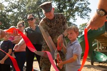 U.S. Marine Col. Curtis Ebitz Jr., commanding officer of Marine Corps Air Station New River, assists Bennet Bell, son of Britney Bell, a Resident Advisory Board (RAB) member of Atlantic Marine Corps Communities, with cutting a ribbon on MCAS New River, Sept. 29, 2021.