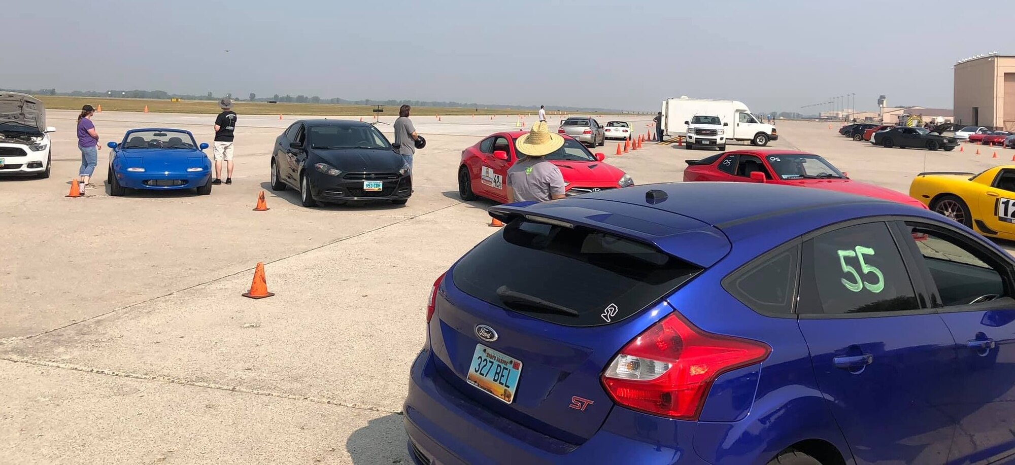 Sports cars are parked in front of a hanger on the flight line.