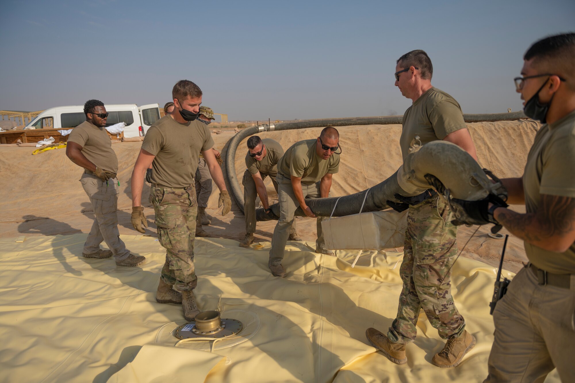 U.S. Airmen with the 332nd Logistics Readiness Squadron attach hoses to a collapsible fabric tank