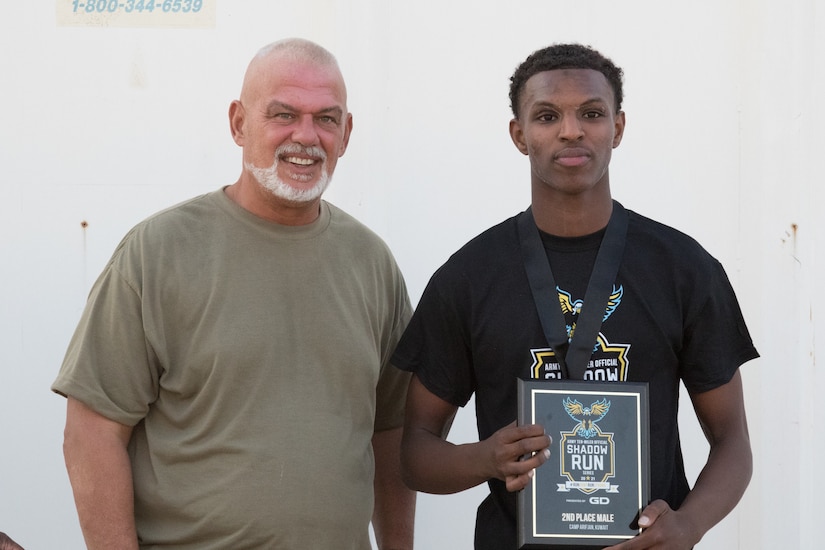 Spc. Yacob I. Warsame, a signal support systems specialist assigned to 3rd Expeditionary Sustainment Command, stands with Roger Disbrow, the morale, welfare, and recreation director, after placing second in the Army Ten-Miler Shadow Run at Camp Arifjan, Kuwait, on Oct. 10, 2021. The Denver, Colo., native, currently deployed in support of the 1st Theater Sustainment Command Operational Command Post, said the Army has helped him unlock his potential.