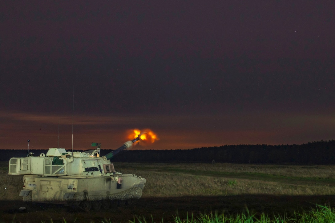 Soldiers fire an armored vehicle in the woods.