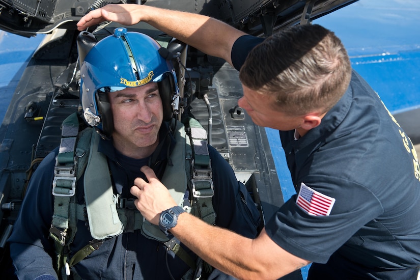 A man is strapped into a jet by another man.