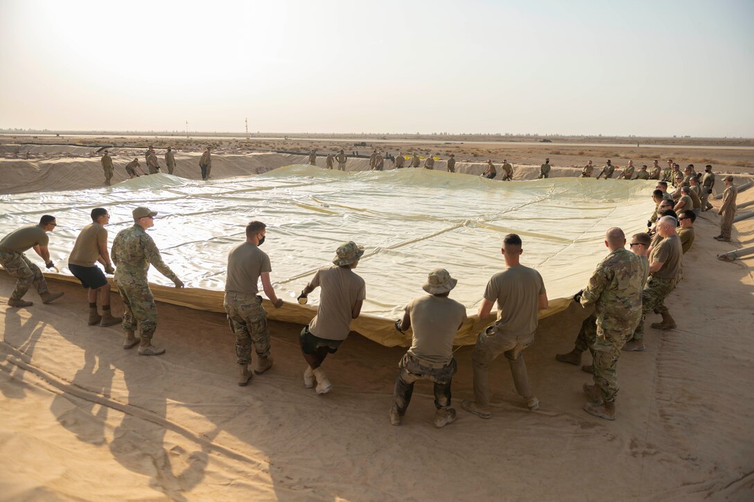 Airmen spread out collapsible fabric in a desert.