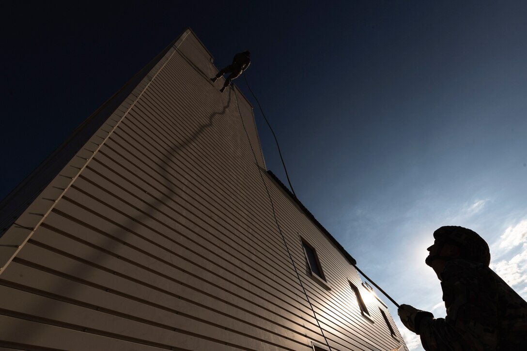 An American airman secures a rope as a Lithuanian soldier rappels down a structure as shown in silhouette.