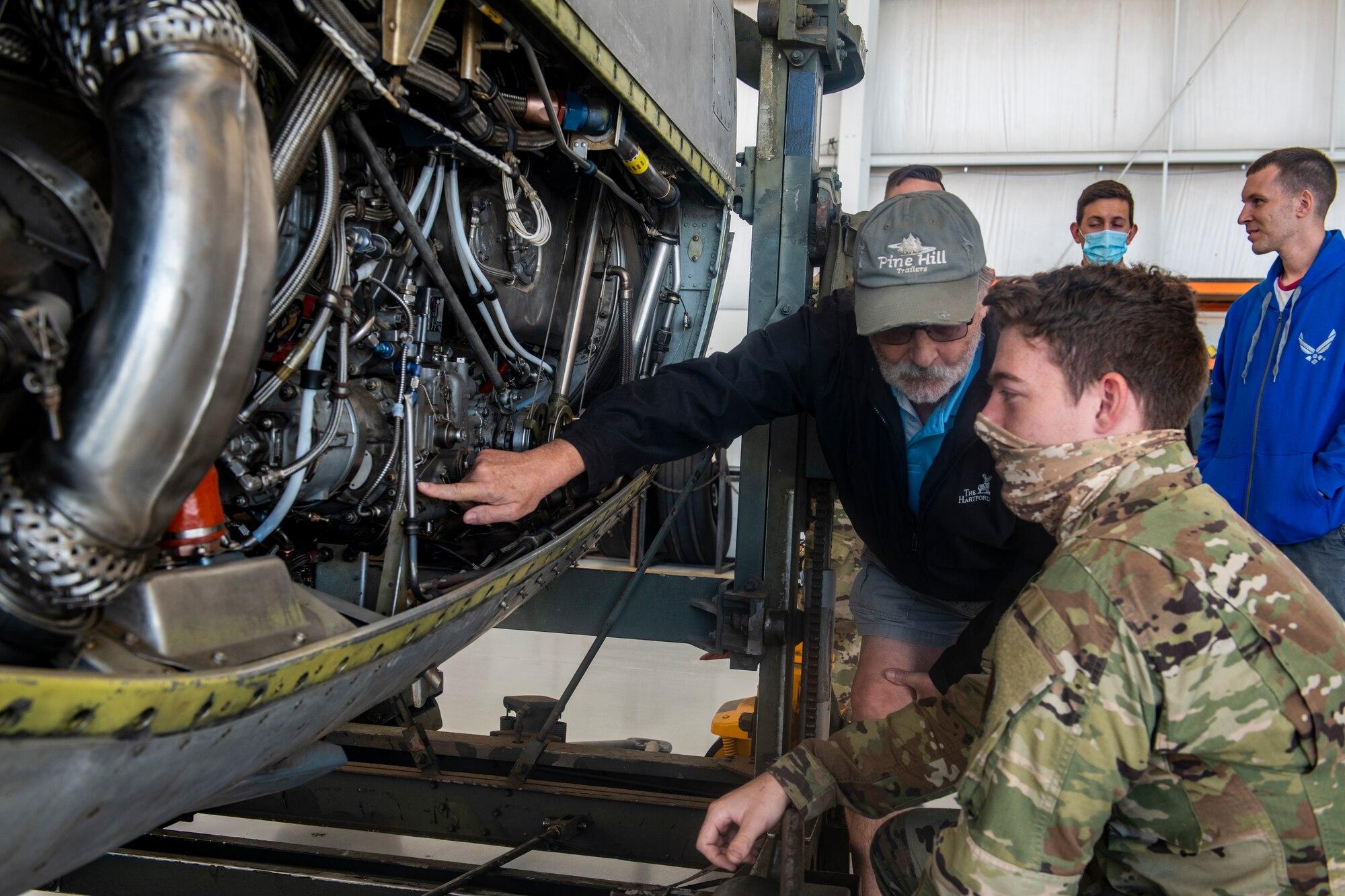A civilian retiree and an active duty airman look at an aircraft engine.