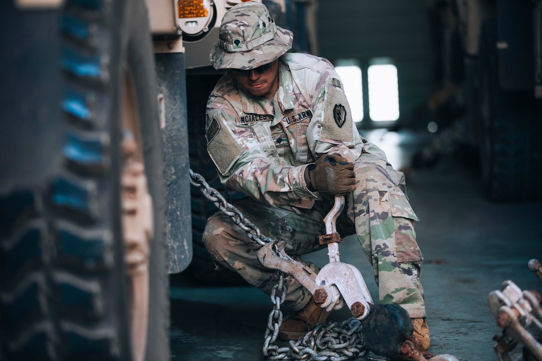 A soldier secures a chain attached to a military vehicle.